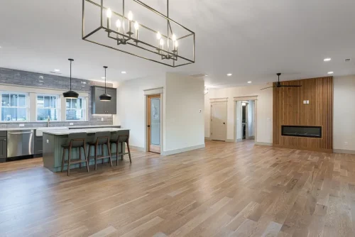 Open-concept kitchen and living space with wood flooring, a large island, and a slatted wood fireplace wall.