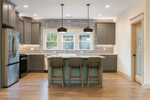 Kitchen with gray cabinetry, green island, white countertops, stainless steel appliances, and black pendant lights.