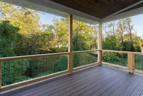 Covered rear deck with wood posts, cable-style railing, and views of the surrounding trees.