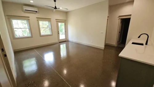 Open lower-level space with polished concrete floors, a kitchenette, large windows, and an exterior door.