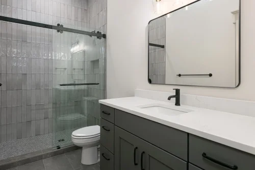 Bathroom with dark cabinetry, white countertop, black fixtures, and a glass-enclosed tiled shower.
