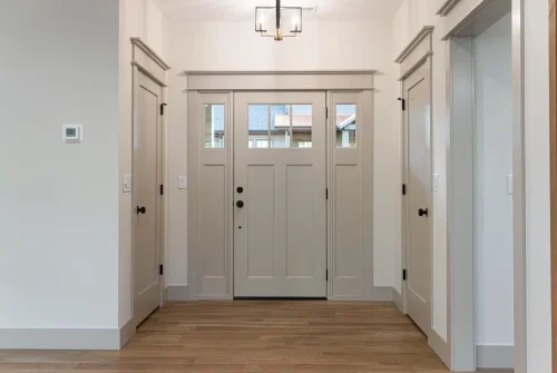 Front entry with a paneled door, sidelights, wood flooring, and neutral trim.