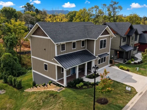 Aerial view of a two-story home with taupe vertical siding, white trim, gabled rooflines, and a covered front porch.