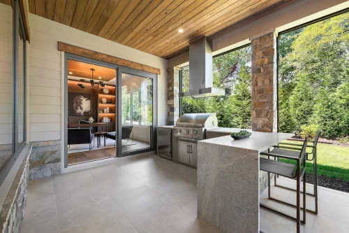 Outdoor kitchen with grill, bar seating, and view into office.