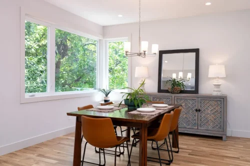 Dining area with wood table, leather chairs, large windows, and buffet with mirror.