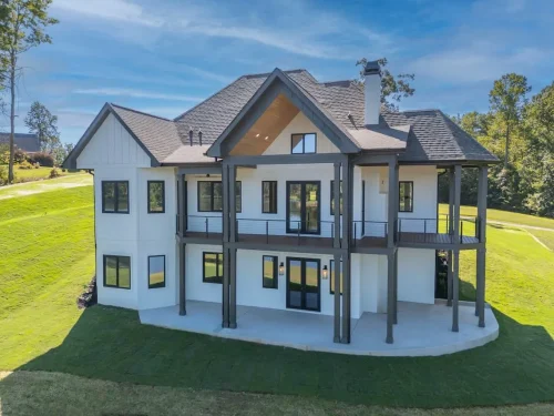Two-story lakeside home featuring white siding, dark trim, large windows, and a covered patio supported by tall columns.d