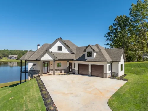 Lakeside home with white siding, dark gabled rooflines, an attached two-car garage, and a spacious concrete driveway.