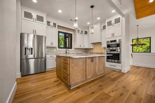 Bright kitchen with white cabinetry, a natural wood island, stainless steel appliances, pendant lighting, and wide-plank wood floors.