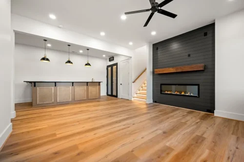 Spacious entertainment room featuring a built-in bar, black accent fireplace wall, wood flooring, and recessed lighting.