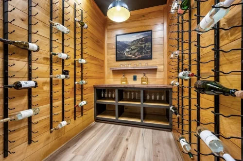 Wood-paneled wine room with black metal bottle racks, a built-in counter, open shelving, and decorative lighting.