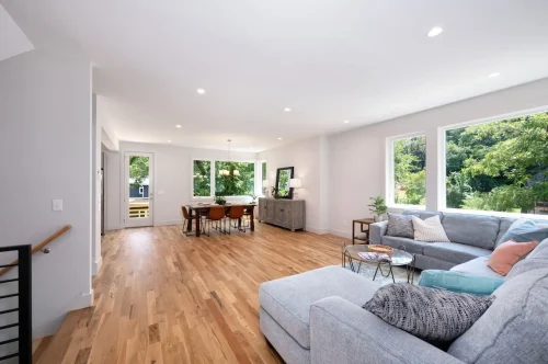 Open-concept living and dining space with wood floors, natural light, and comfortable gray sectional.