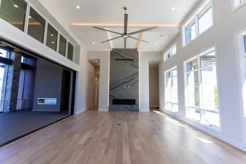 Spacious living area with a floor-to-ceiling stone fireplace, large windows, wood flooring, and an opening to the covered deck.