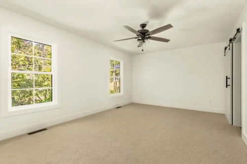 Empty bedroom with white walls, beige carpet, and ceiling fan.