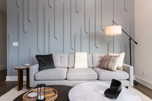 Sitting area with a gray sofa, layered round coffee tables, and a tall geometric accent wall.