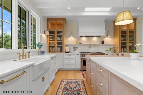 Renovated kitchen with white cabinetry, natural wood accents, marble countertops, brass fixtures, and a large center island.
