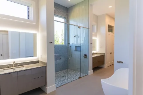 Modern bathroom with a glass-enclosed tiled shower, floating vanities, illuminated mirrors, and a freestanding tub.