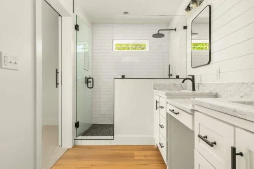 Bathroom with white cabinets, marble countertops, and glass shower.