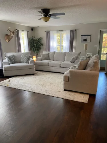 Cozy living room with neutral furniture, dark wood floors, and large windows.
