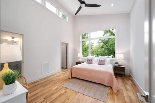 Primary suite with vaulted ceiling, large windows, and soft pink bedding.