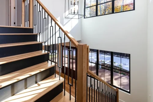 Wood staircase with black metal railings, large windows, and a modern pendant light.
