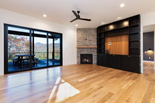 Living room with hardwood floors, a stone fireplace, built-in cabinetry, and sliding doors opening to a mountain-view deck.