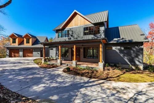 Mountain home with dark siding, wood accents, a metal roof, covered front porch, and detached garage.