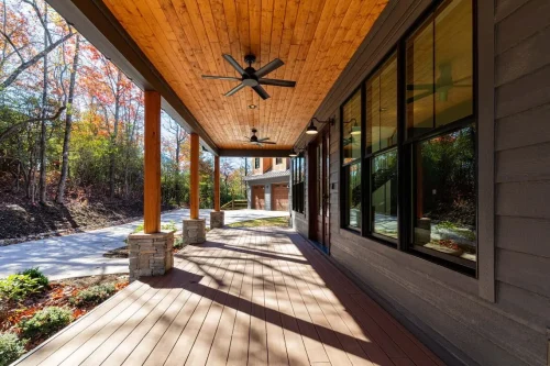 Covered front porch with wood ceiling and columns, stone bases, and large black-framed windows.