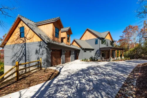 Front exterior showing the home and detached garage with dark siding, wood accents, and metal roofs.
