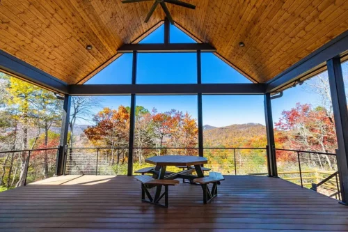 Screened porch with a vaulted wood ceiling, picnic table, and expansive mountain views.