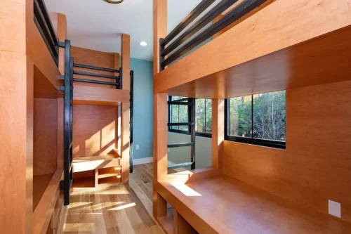 Custom built-in wood bunk beds with black metal ladders, integrated storage, and large windows.