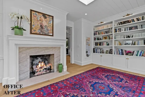 Renovated office with a marble-surround fireplace, built-in white bookshelves, a colorful area rug, and wood flooring.