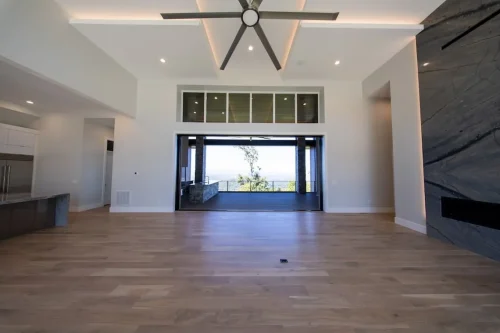 Open living area with a tall ceiling, modern fireplace, wood flooring, and wide opening to a covered outdoor living space.