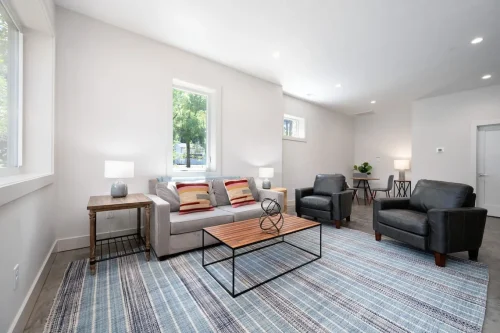 Basement living area with sofa, chairs, blue striped rug, and desk nook.