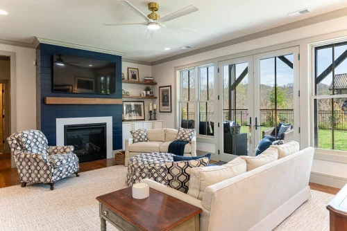 Bright family room with navy shiplap fireplace, mounted TV, French doors, and cozy neutral seating with patterned ottoman.