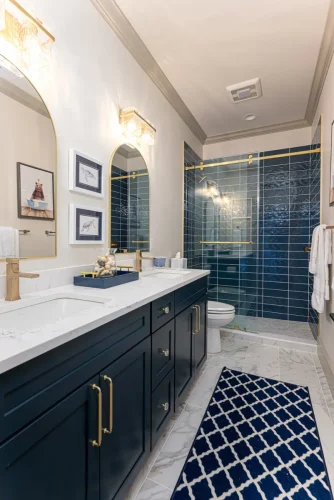 Stylish bathroom with navy double vanity, marble countertops, arched mirrors, and a glass shower with glossy navy tile.