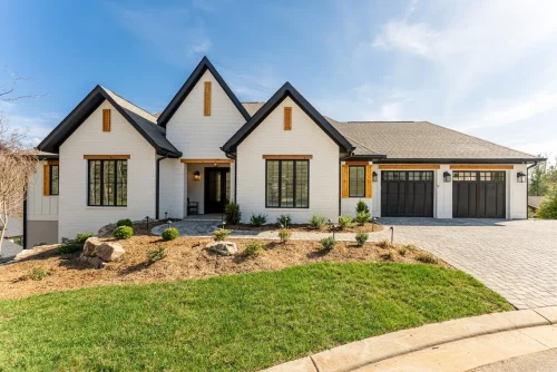 White painted brick home with black trim, wood shutters, and a three-car garage, set on a landscaped lot with a paved driveway.