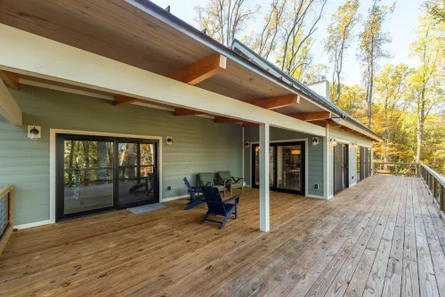 Spacious covered wood deck with multiple sliding glass doors and views of the surrounding trees.