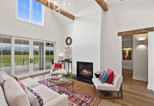Living space of Ecusta Farmhouse, windows showing outdoors, and letting int lots of light. Clean basic design, fireplace, white couches and chairs. 
