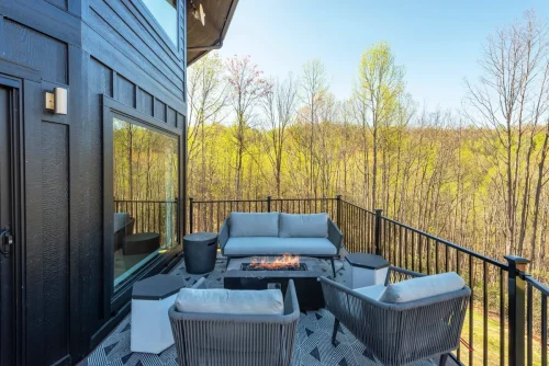 Balcony with sleek black siding, cushioned lounge seating, and a rectangular fire table overlooking wooded mountain views.