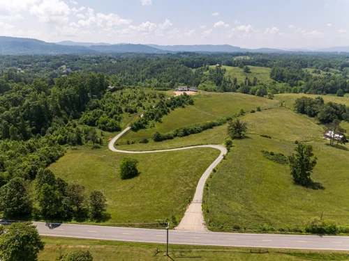 Aerial view of Highland Ridge Farm showing winding driveway leading to estate home, surrounded by rolling green pastures and mountain backdrop.