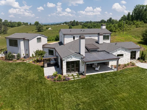 Back exterior of Highland Ridge Farm with multiple chimneys, covered patios, stone detailing, and manicured lawn.
