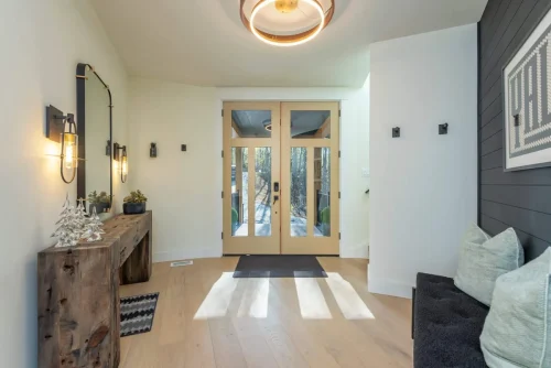 Bright foyer with glass double doors, wood console table, wall mirror, and modern lighting accents