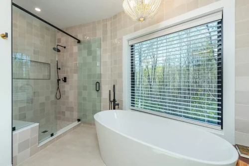 Luxury bath with soaking tub, walk-in glass shower, tiled walls, and a large window with wooded views.
