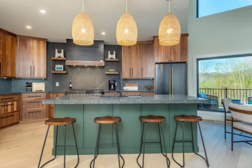 Chef’s kitchen with dark countertops, green island with barstools, walnut cabinetry, and pendant lighting.