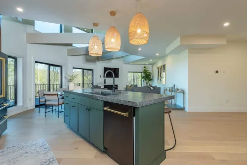 Open kitchen with island seating, woven pendant lights, and expansive windows leading to outdoor deck.