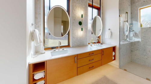 Arcadian Abode bathroom with wood double sink vanity and glass shower door.