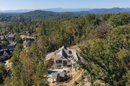 Aerial view of a mountain home nestled among trees, featuring a multi-level design, outdoor pool, and expansive mountain views.