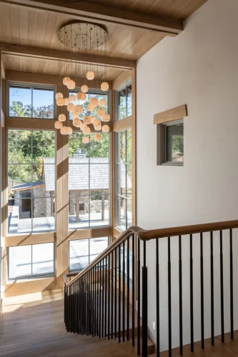 Staircase featuring natural wood handrails, black metal balusters, floor-to-ceiling windows, and a cascading globe pendant chandelier.