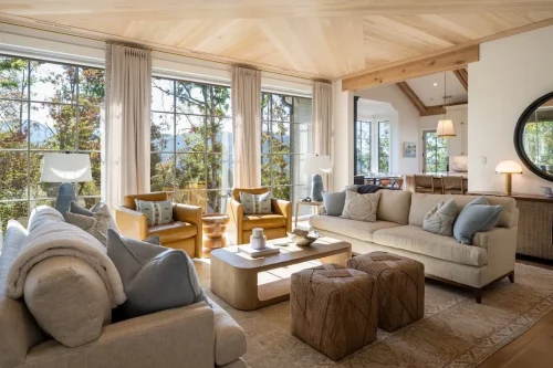 Bright living room with large windows overlooking the mountains, neutral furnishings, natural wood ceiling, and upholstered seating.