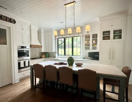 Spacious white kitchen with large island, pendant lighting, farmhouse sink, and wall of windows.